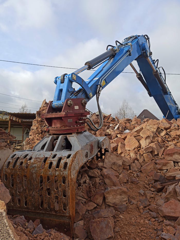 Heavy machinery with a hydraulic claw handling large piles of debris and rocks.