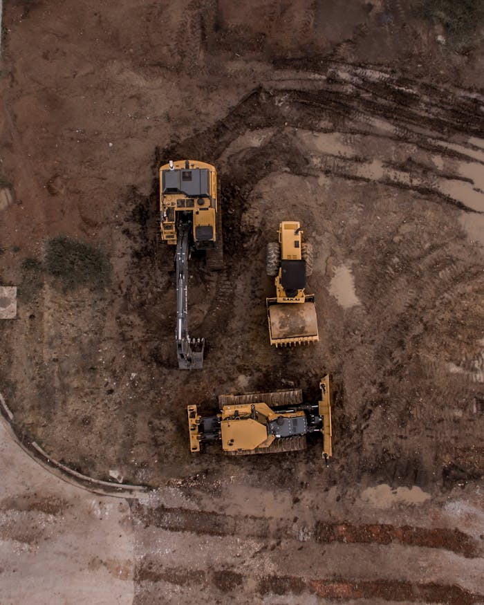 Aerial view of heavy machinery, including excavators and bulldozers, on a dirt site for land development.