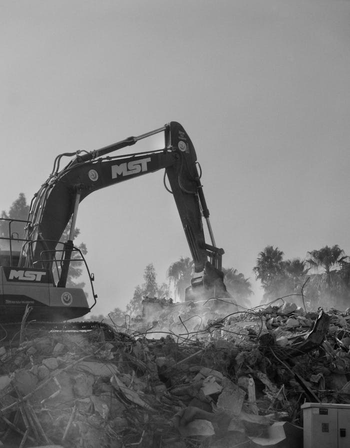 Excavator tearing down a house structure amidst debris for demolition.